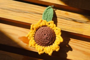 Un porte clé au crochet en forme d'amigurumi, posé à côté du fil et du crochet utilisés pour le réaliser